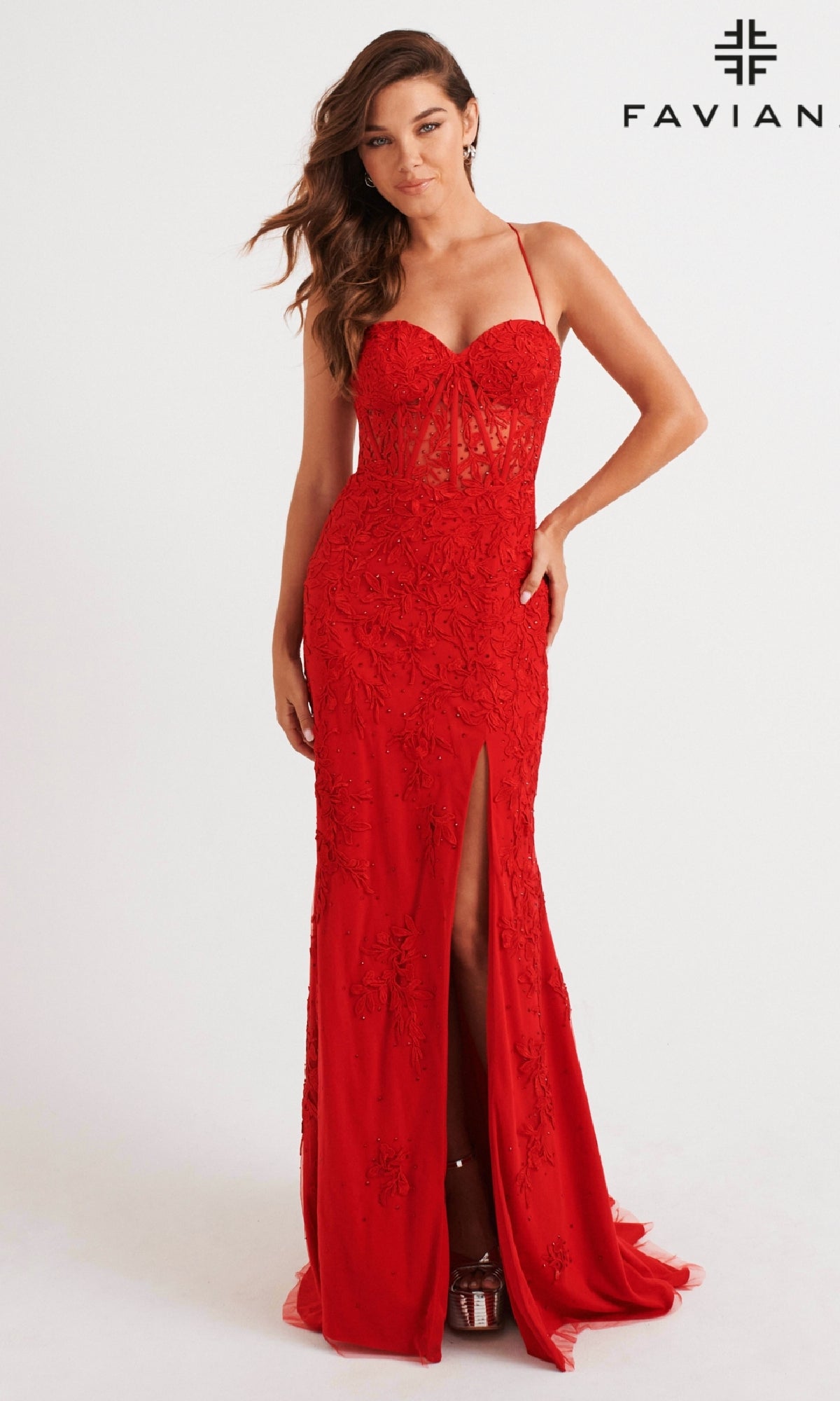 A woman wearing the Lace-Applique Long Faviana Prom Dress 11054, featuring thin straps, a floral lace bodice, and a high leg slit, stands against a plain background with the Faviana logo.